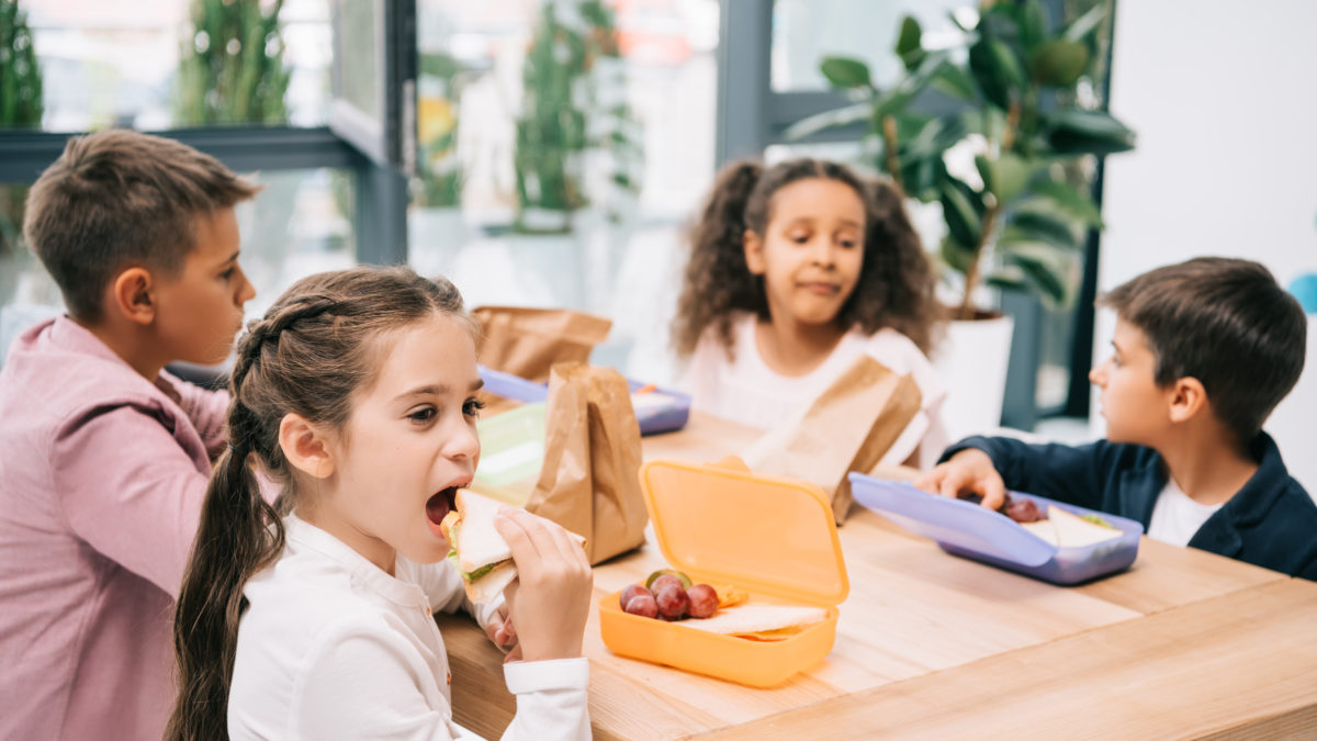 schoolkids eating healthy school lunch while sitting toget