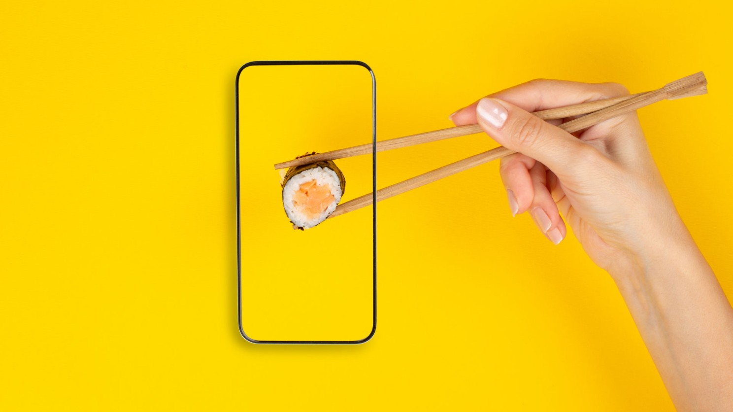 A hand reaches in from the edge of the image, picking up sushi with a pair of chopsticks. The sushi roll is inside a smart phone, representing healthy food delivery via an app